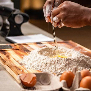 Cracking an egg into a pile of flour on a wooden chopping board in a kitchen setting.
