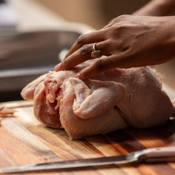 Close-up of a hand preparing a whole chicken on a wooden cutting board for cooking.