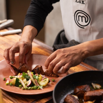 A chef plating a gourmet dish with sliced meat and fresh vegetables on a rustic wooden table.