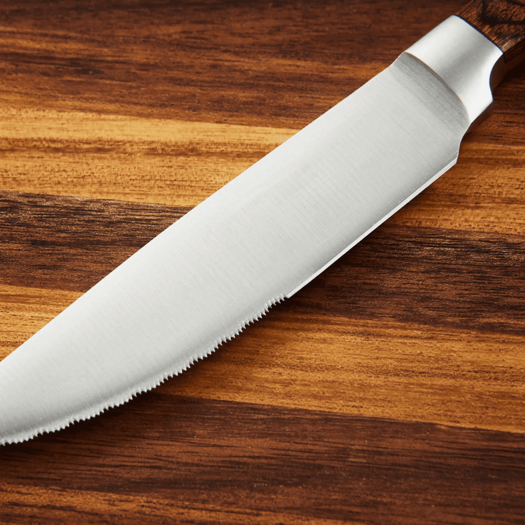 Close-up of a razor-sharp stainless steel steak knife blade on a wooden table.