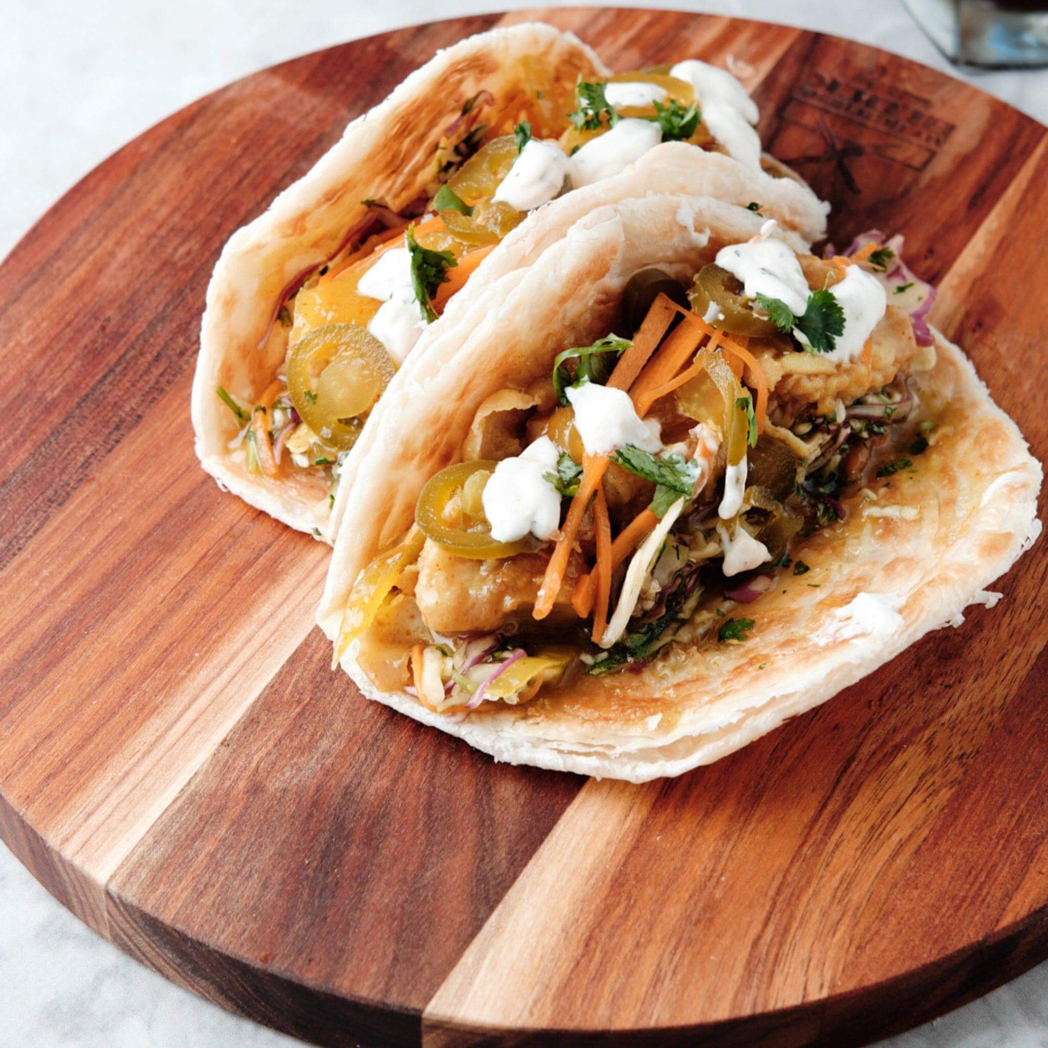 Two delicious tacos topped with fresh ingredients served on a wooden round chopping board.