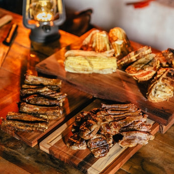 Grilled meats and corn displayed on wooden boards with a lantern in a rustic setting.