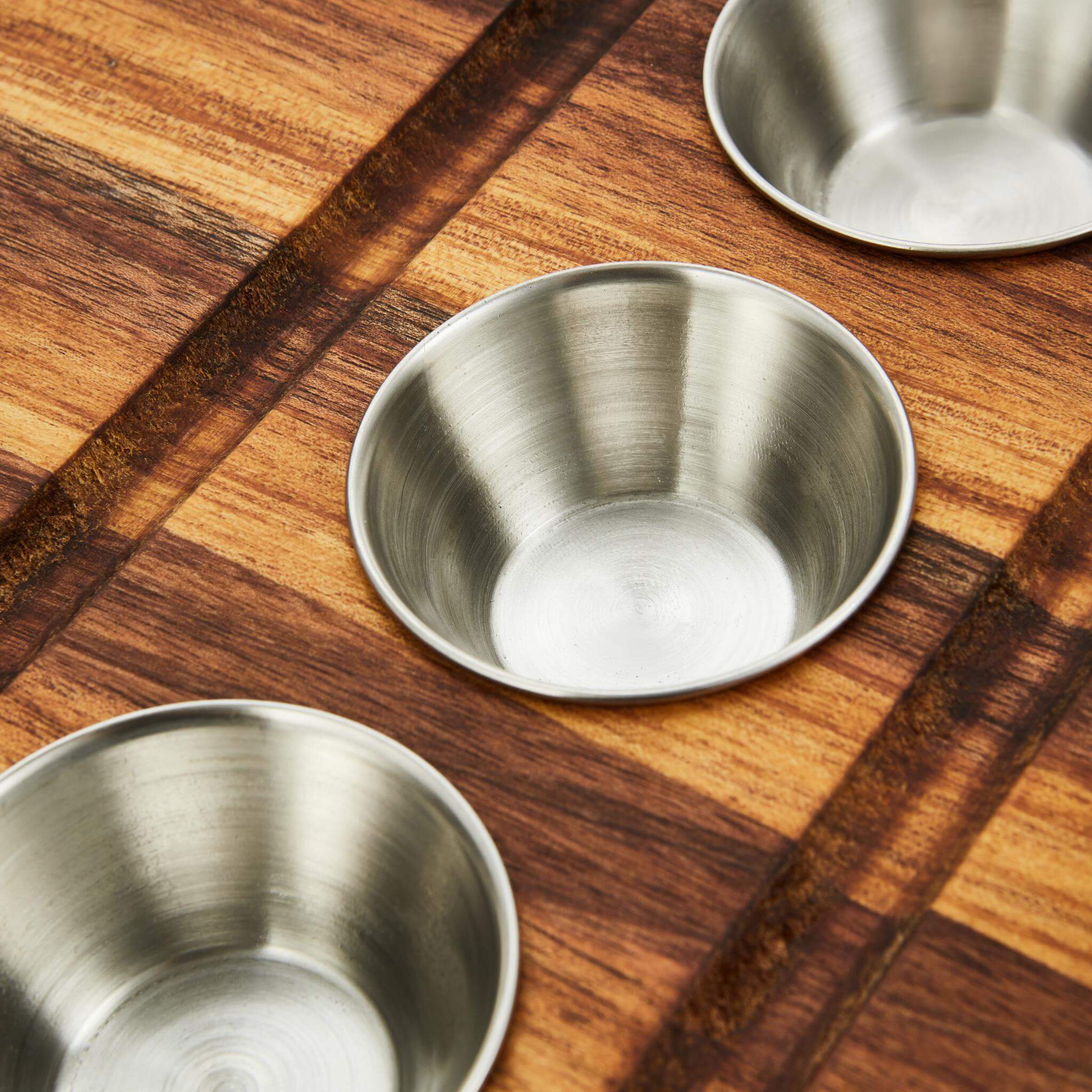 Three stainless steel bowls arranged on a wooden meat board, perfect for seasoning at a braai.