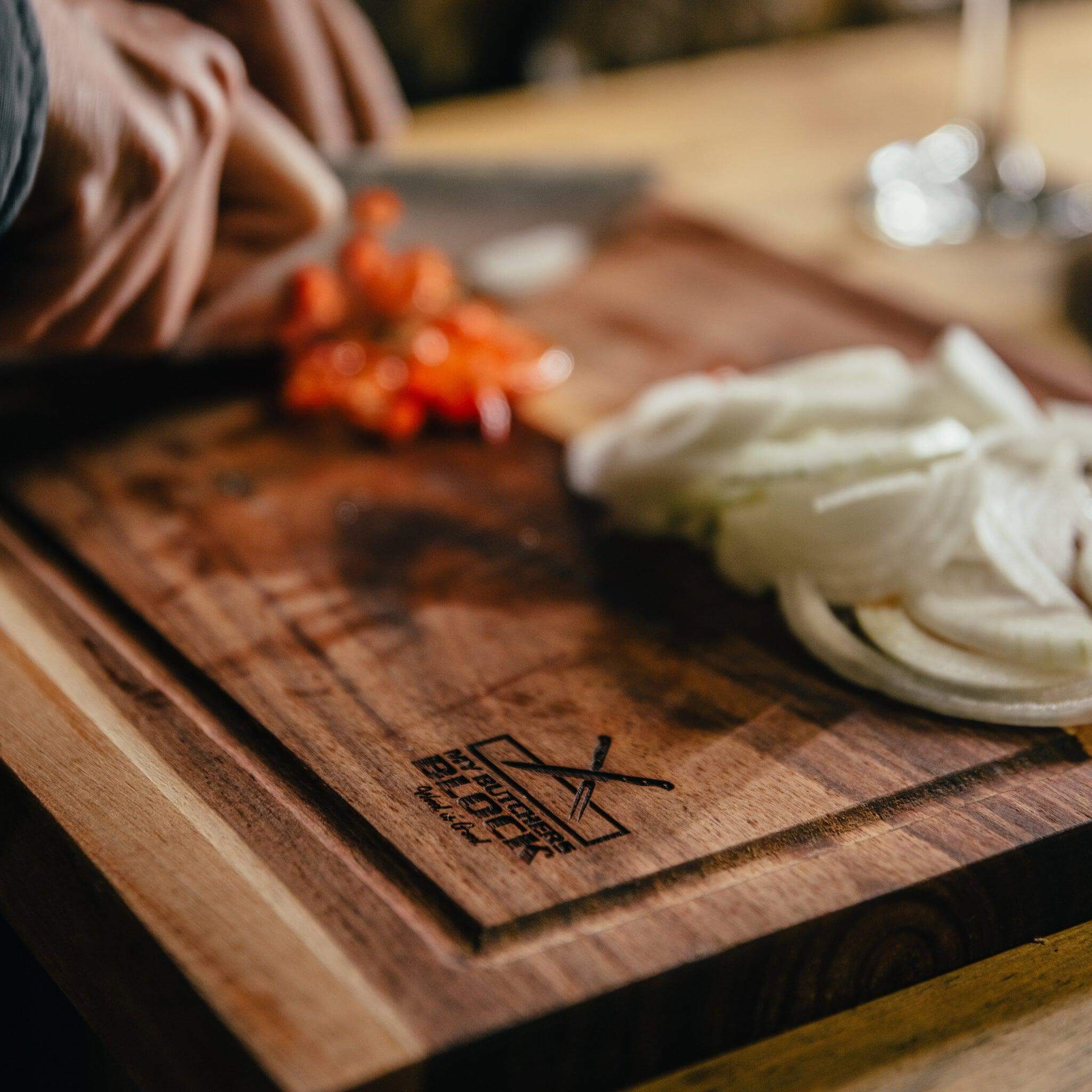 Person chopping onions and tomatoes on a wooden chopping board with lip, showcasing precision and stability in the kitchen.