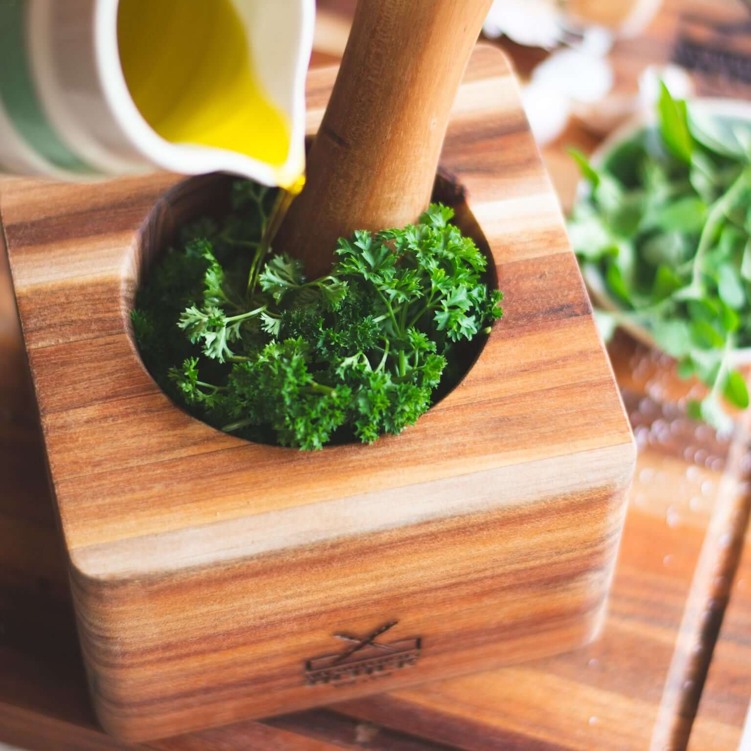Wooden pestle and mortar filled with fresh herbs, ideal for grinding and blending ingredients in the kitchen.