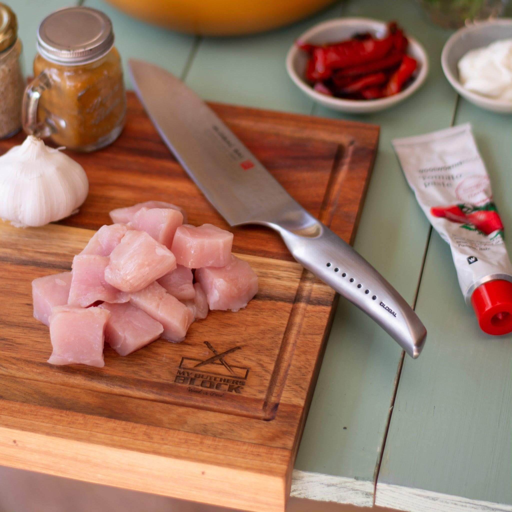 Chopped chicken on a chopping board with a knife and other ingredients, ideal for meal prep.