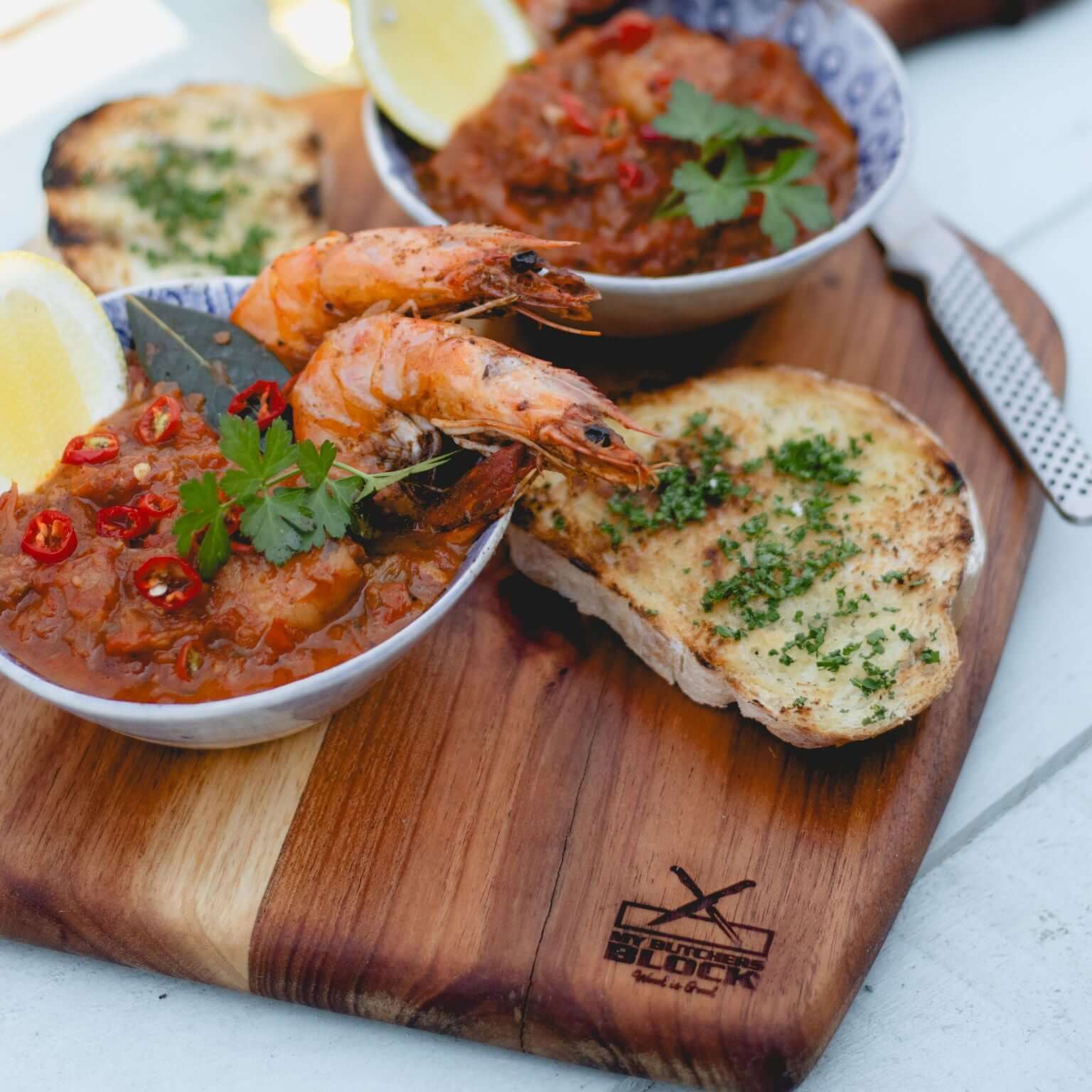 Delicious shrimp and seafood dish served on a stylish wooden nesting board with toast and garnishes.