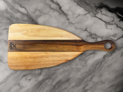 Wooden serving paddle with a natural finish and a hole in the handle, set against a marble background.