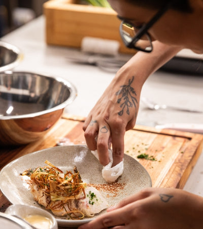 Chef garnishing a dish with crispy onions and herbs, showcasing culinary skills in a modern kitchen.