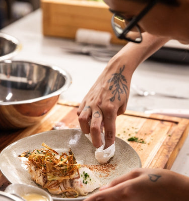 Chef garnishing a dish with crispy onions and herbs, showcasing culinary skills in a modern kitchen.