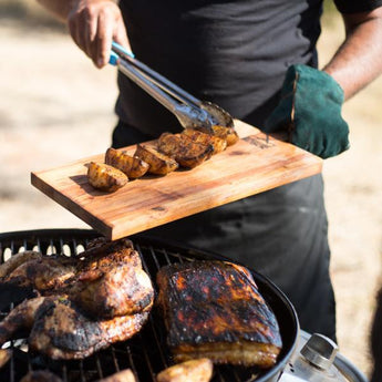 Grilling succulent meats and vegetables on a barbecue with wooden cutting board and tongs in hand.