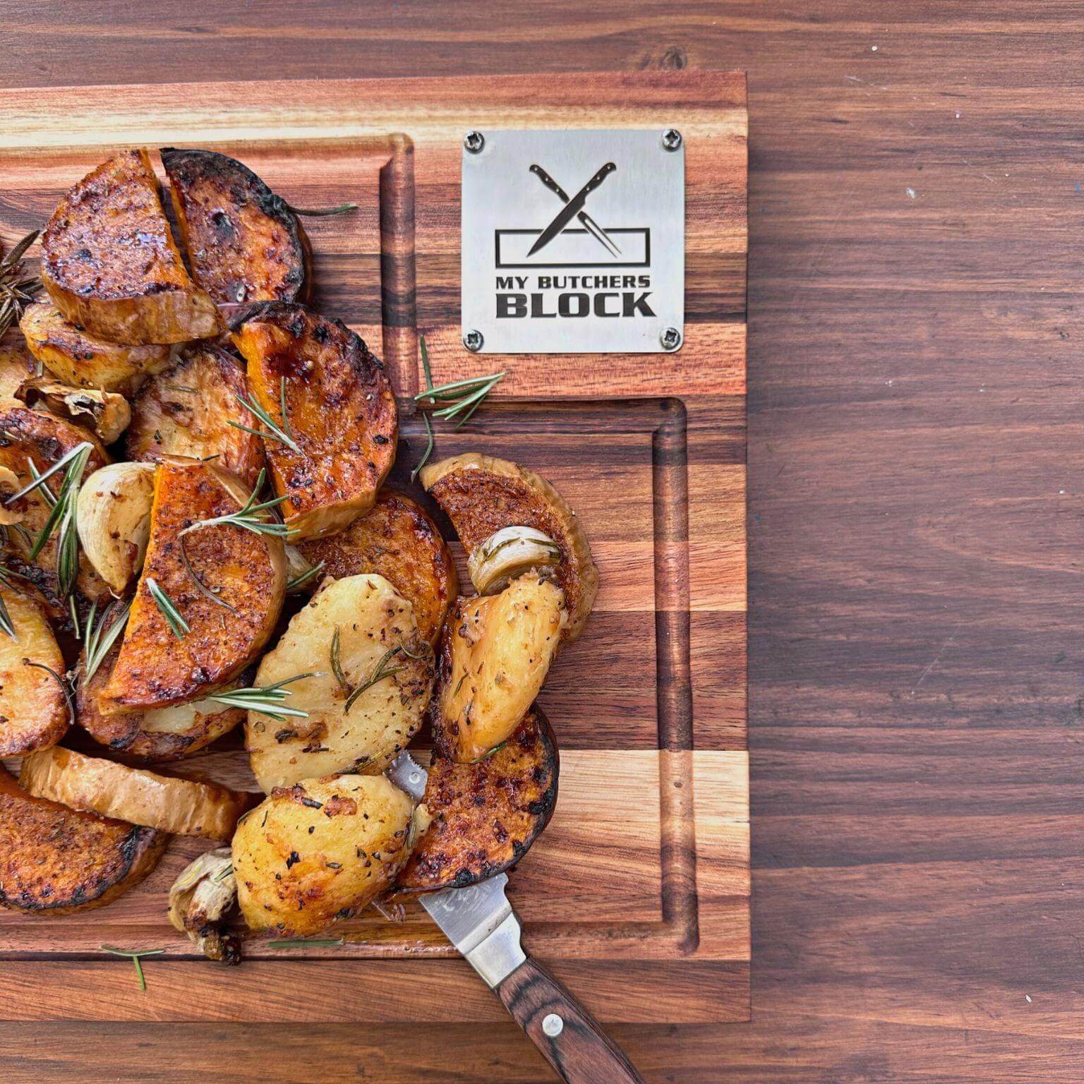 Roasted potatoes on a My Butcher's Block wooden chopping board with a knife and herbs.