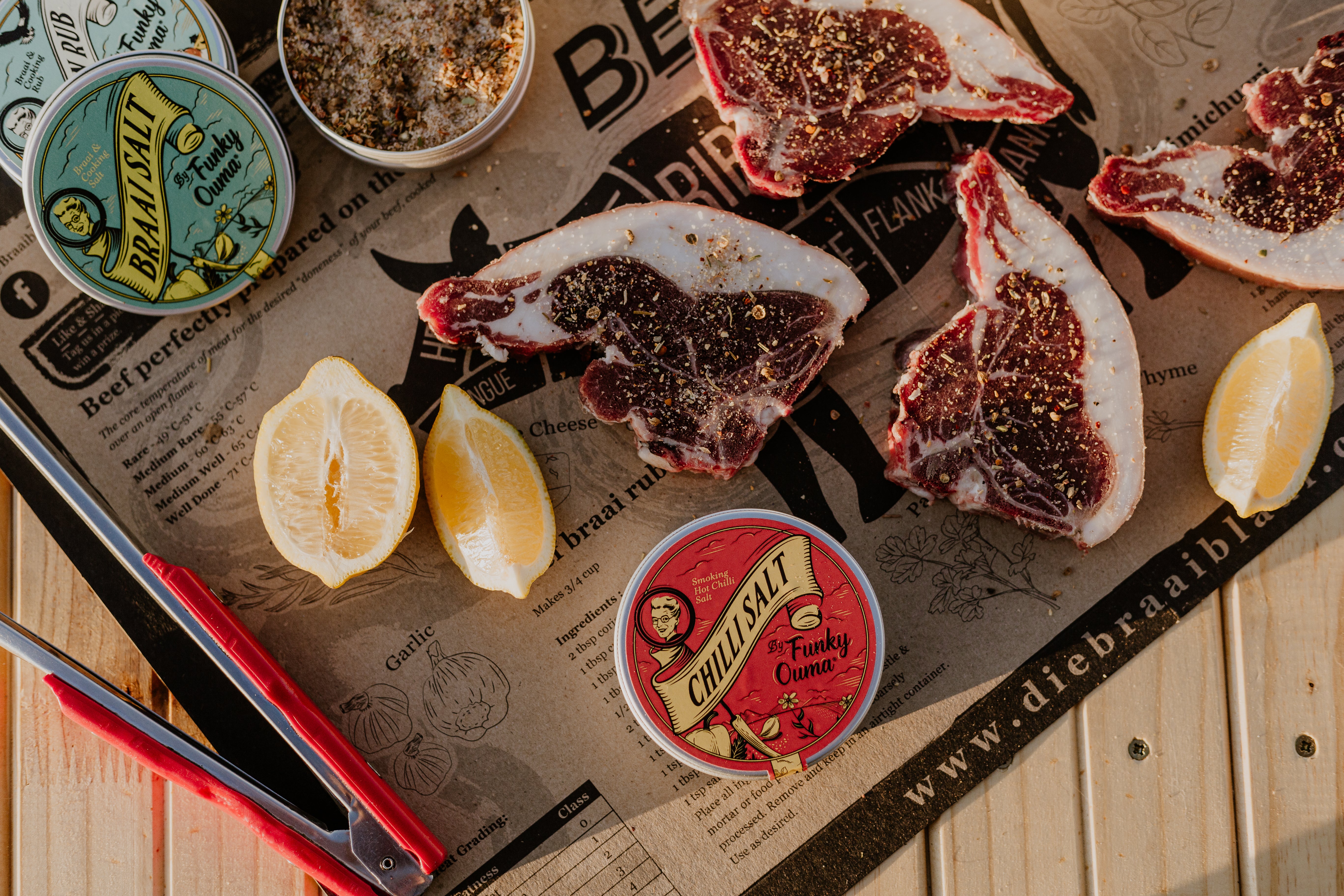 Meat board with seasoned chops, lemon slices, and Funky Ouma Braai spices for outdoor grilling.
