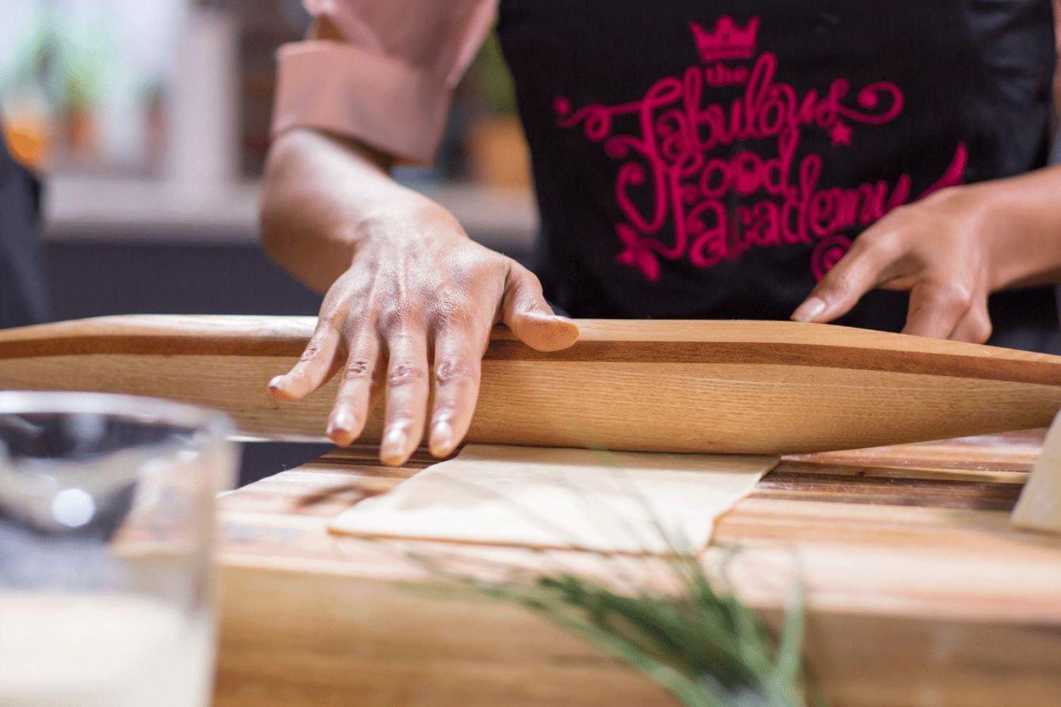 Home baker preparing dough with a handcrafted wooden rolling pin in a cozy kitchen setting.