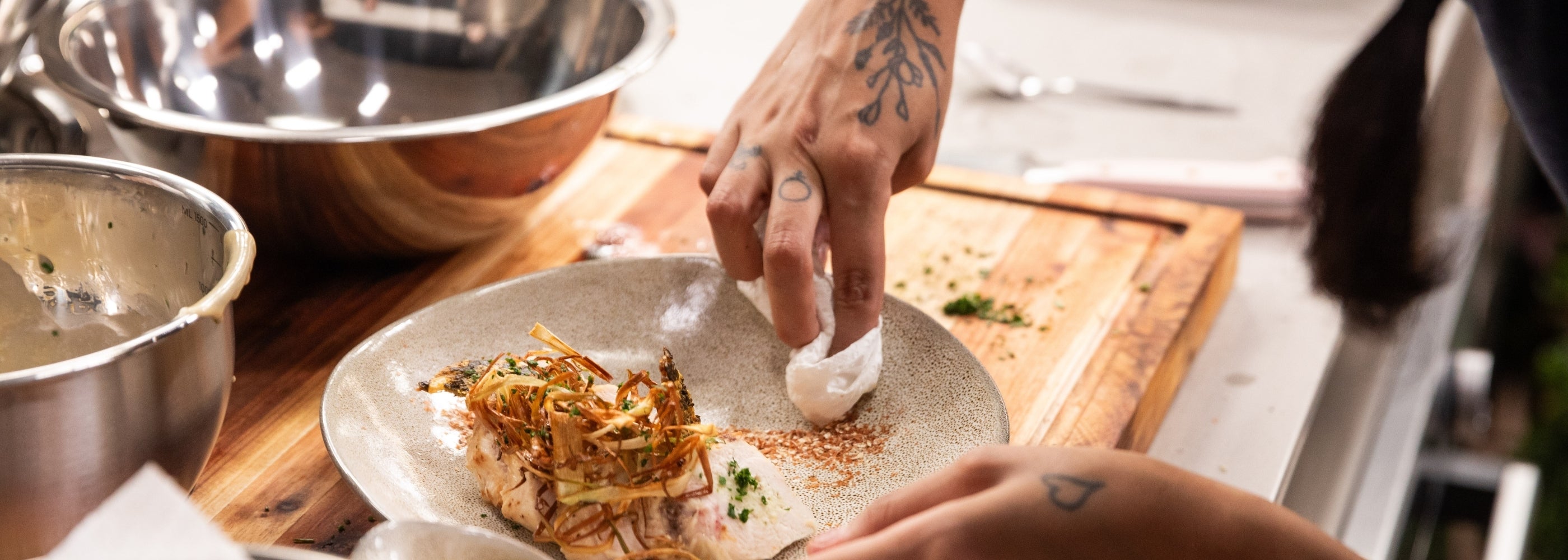 A chef delicately plating a gourmet dish with ingredients on a wooden countertop.