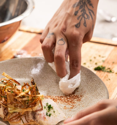 A chef delicately plating a gourmet dish with ingredients on a wooden countertop.
