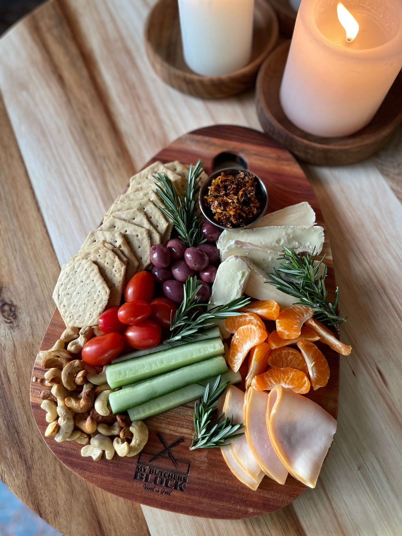 Charcuterie spread on an egg-shaped paddle board, featuring cheese, meats, fruits, and nuts, with candles in the background.