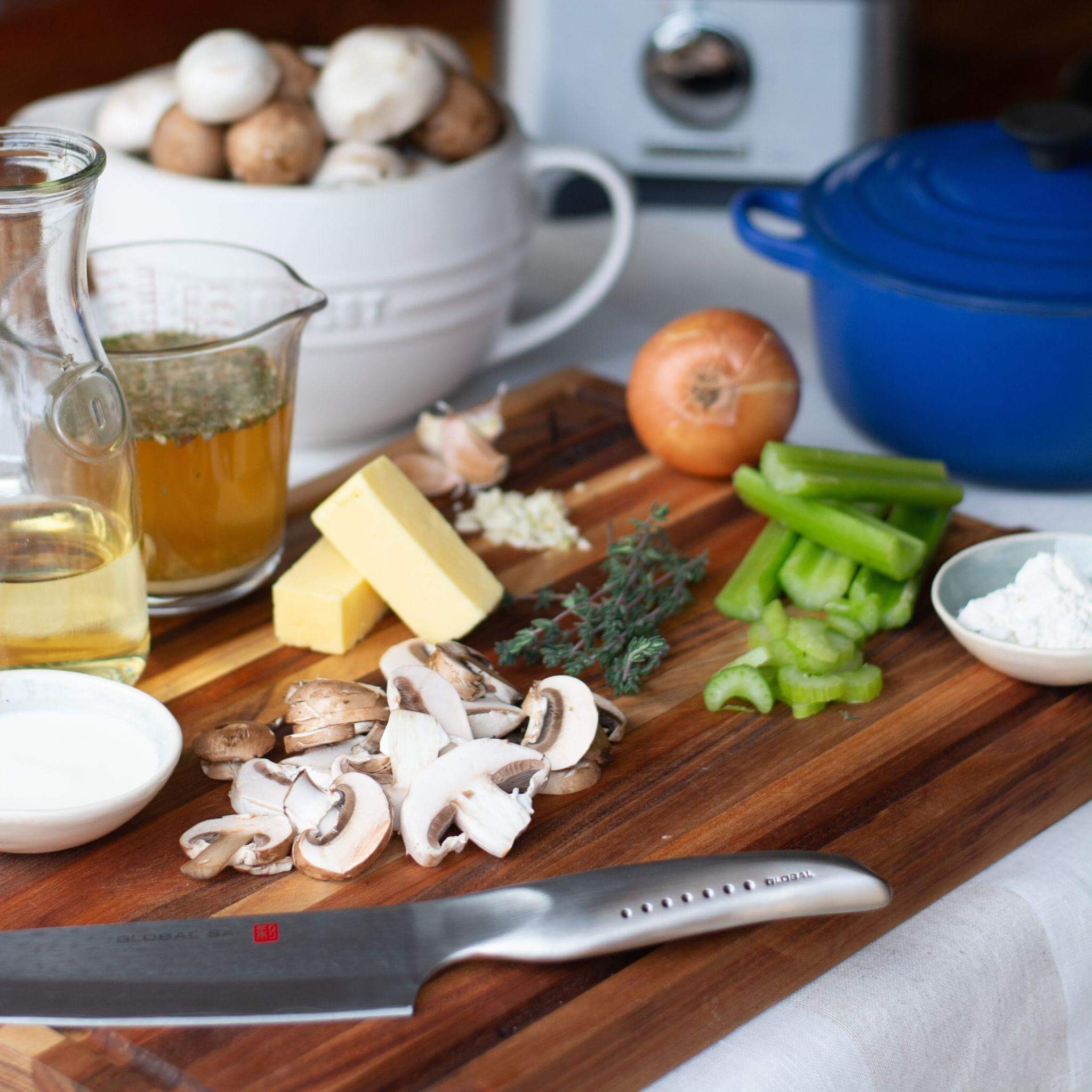 Chopped vegetables, herbs, and ingredients on a large slim chopping block with a chef's knife.
