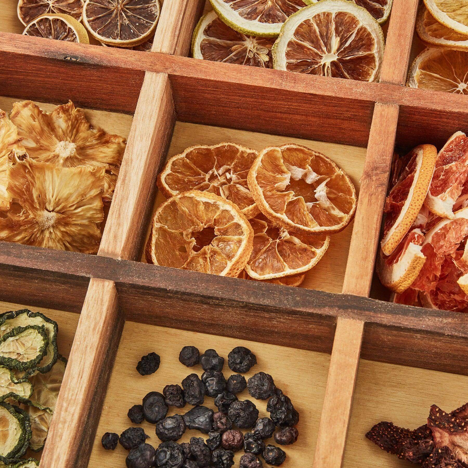 Variety of dried fruits and botanicals in a wooden box, perfect for drink infusions and mixology.