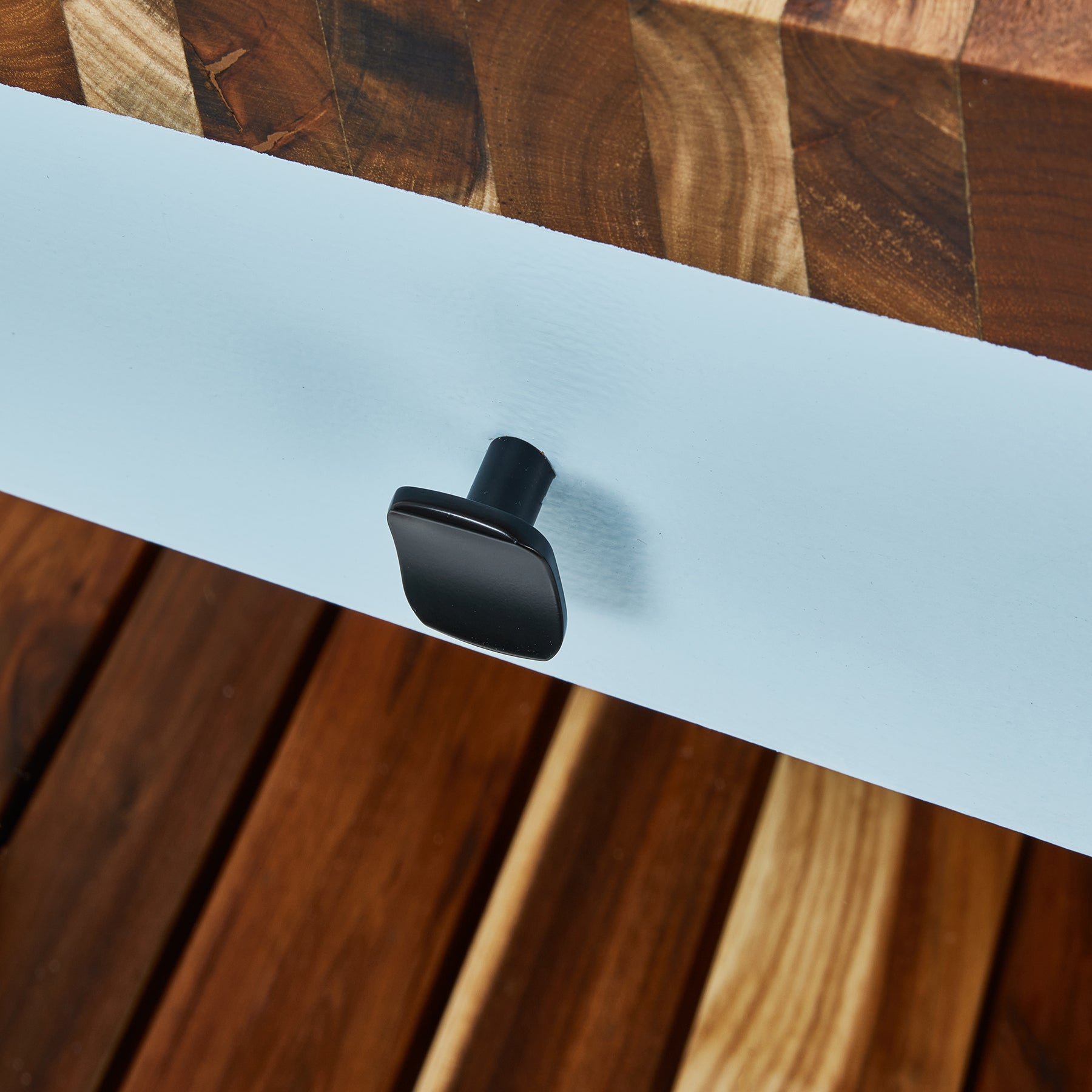 Close-up of a black drawer handle on a compact butcher's bench with wood top and powder-coated steel frame.
