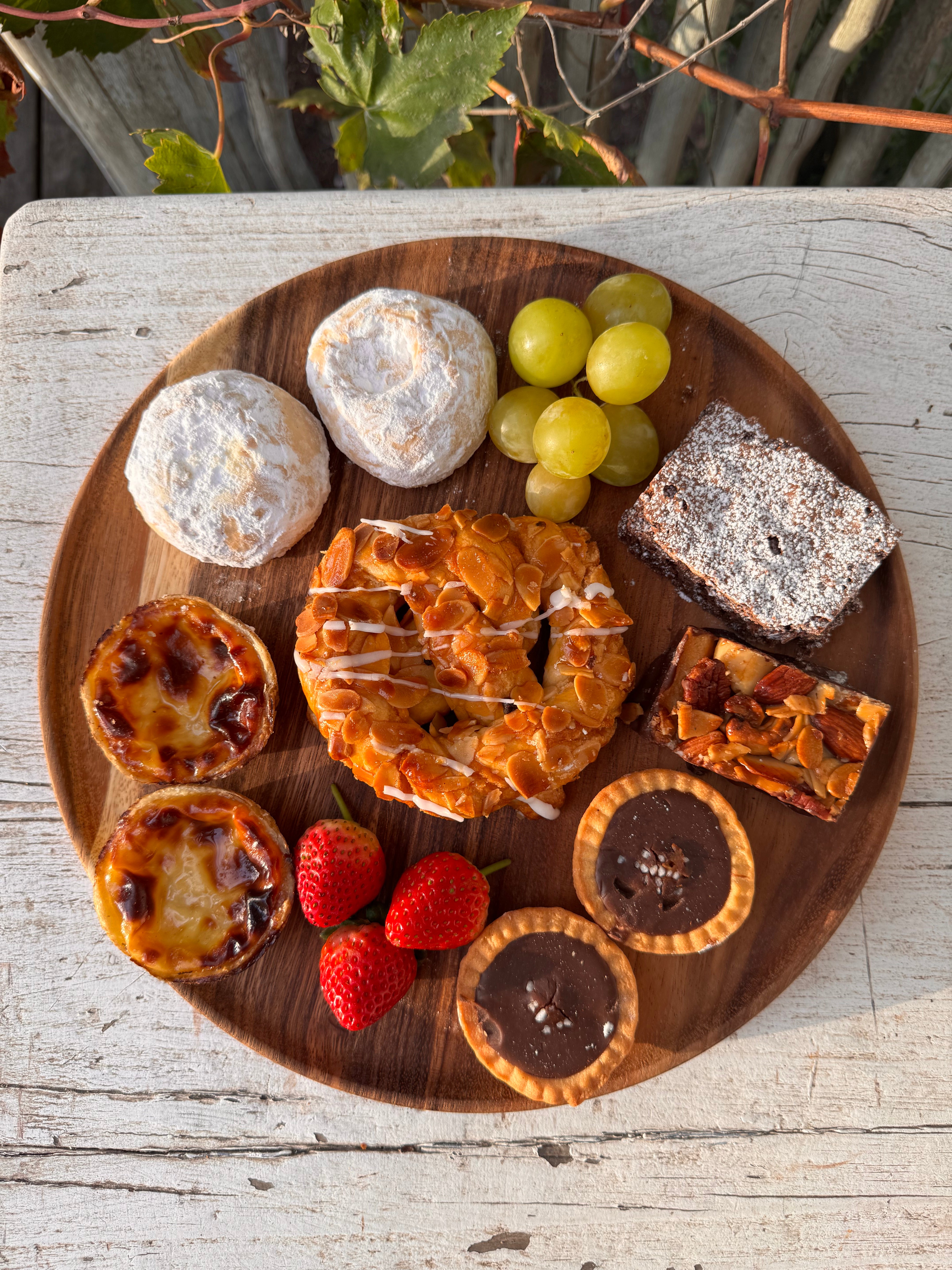 Wooden plate with various pastries and fruits on a rustic wooden surface