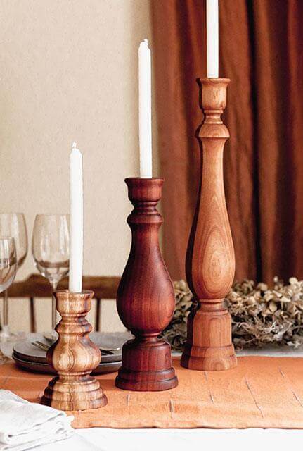 Three handcrafted wooden candlestick holders with white candles, showcasing rustic finishes on a dining table.