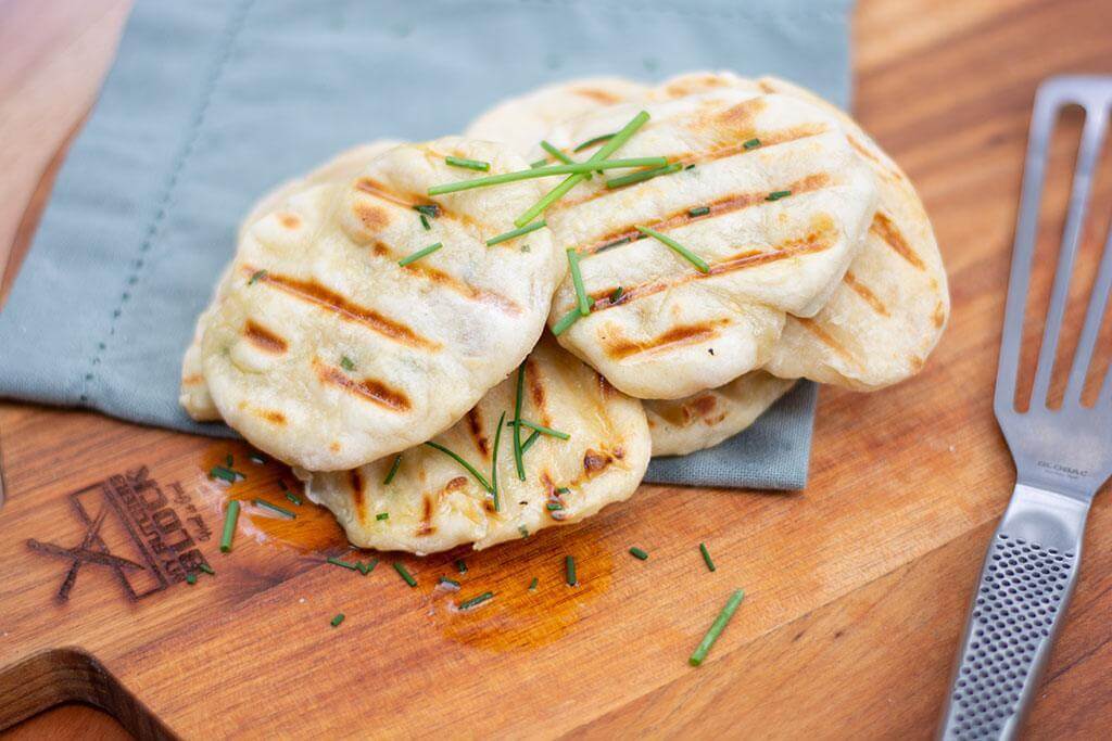 Grilled round flatbreads garnished with chives on a wooden serving board.
