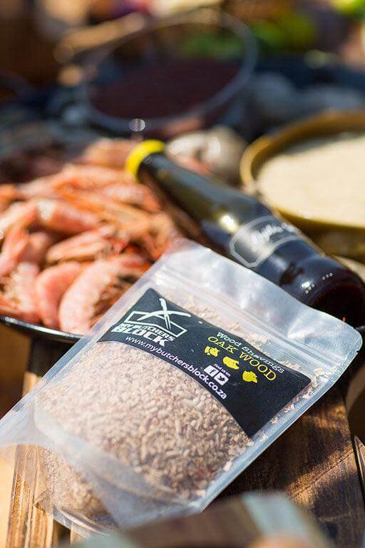 Smoking wood chips in a clear bag next to grilled seafood and drinks, perfect for enhancing smoky flavors.