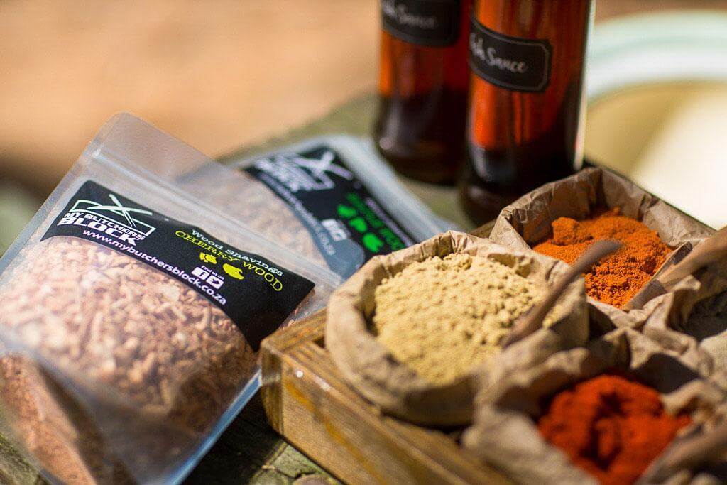 Variety of spices and smoking wood chips displayed in containers for enhancing flavor in cooking.
