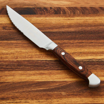 High-quality steak knife with a wooden handle on a wooden cutting board.