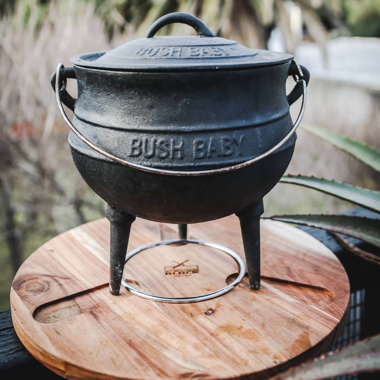 Potjie Stand and Chopping Board featuring a cast iron potjie on a wooden surface, ideal for cooking enthusiasts.