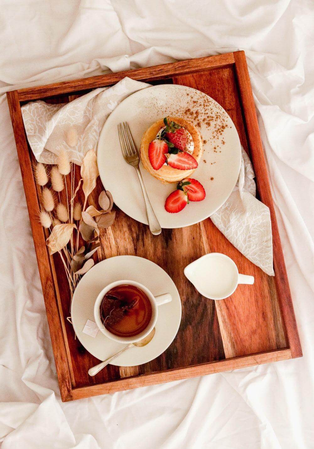 Elegant serving tray with pancake, strawberries, and tea cup on a cozy surface.