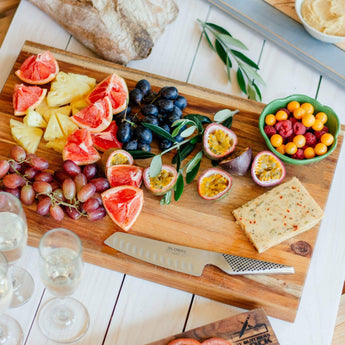 Colorful fruit platter with grapes, pineapple, and citrus on wooden board with knife and glasses of champagne.
