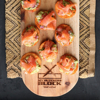 Wooden platter with smoked salmon appetizers topped with guacamole, garnished on a textured black surface.