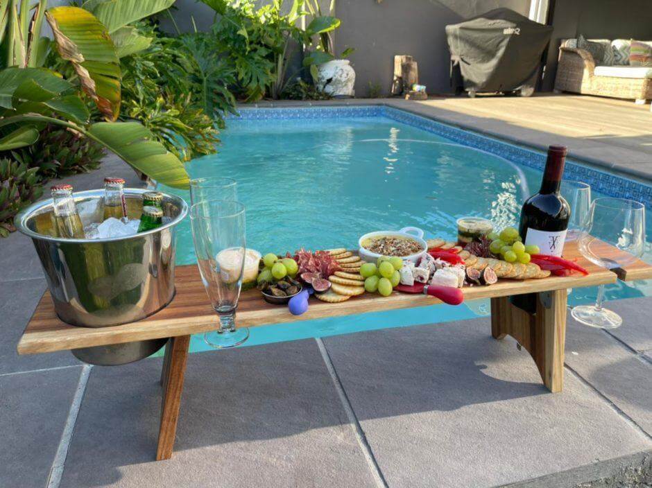 Elegant picnic table by the pool with gourmet food, wine, and drinks, perfect for outdoor gatherings.