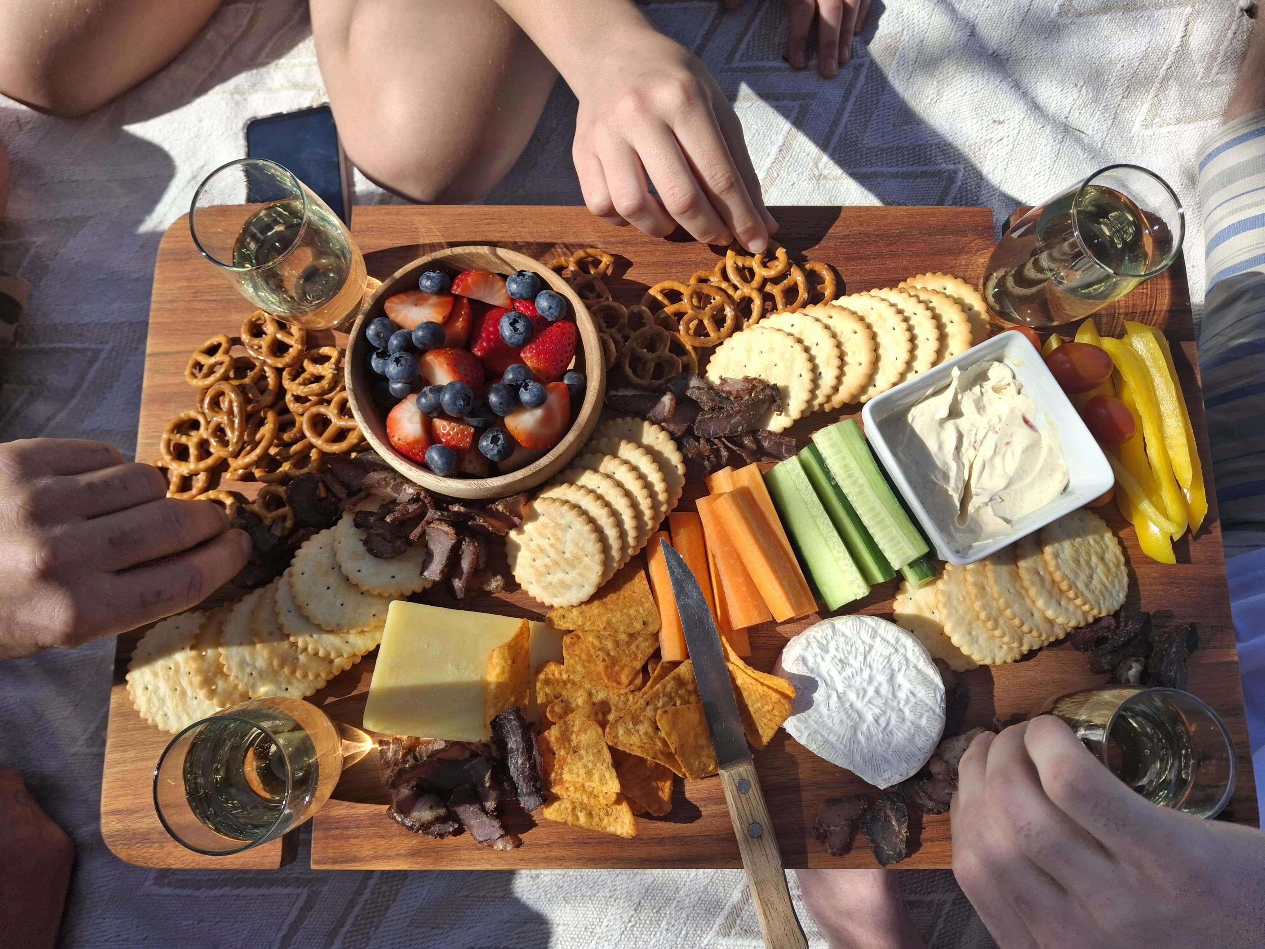 Grazing table featuring assorted cheeses, crackers, fruits, vegetables, and drinks, perfect for entertaining.
