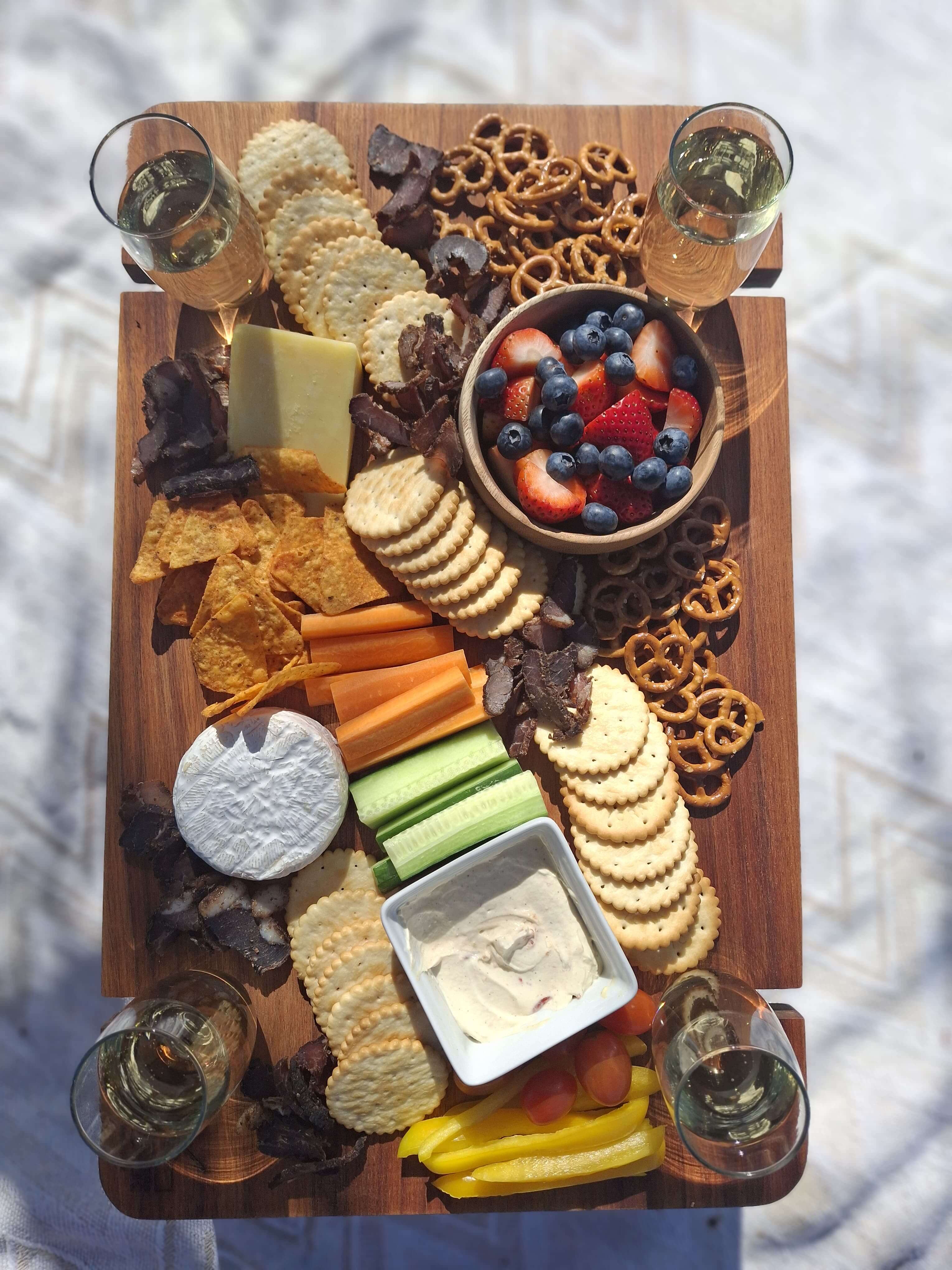 Grazing table filled with crackers, cheese, fruits, and dips, paired with glasses of sparkling beverage.
