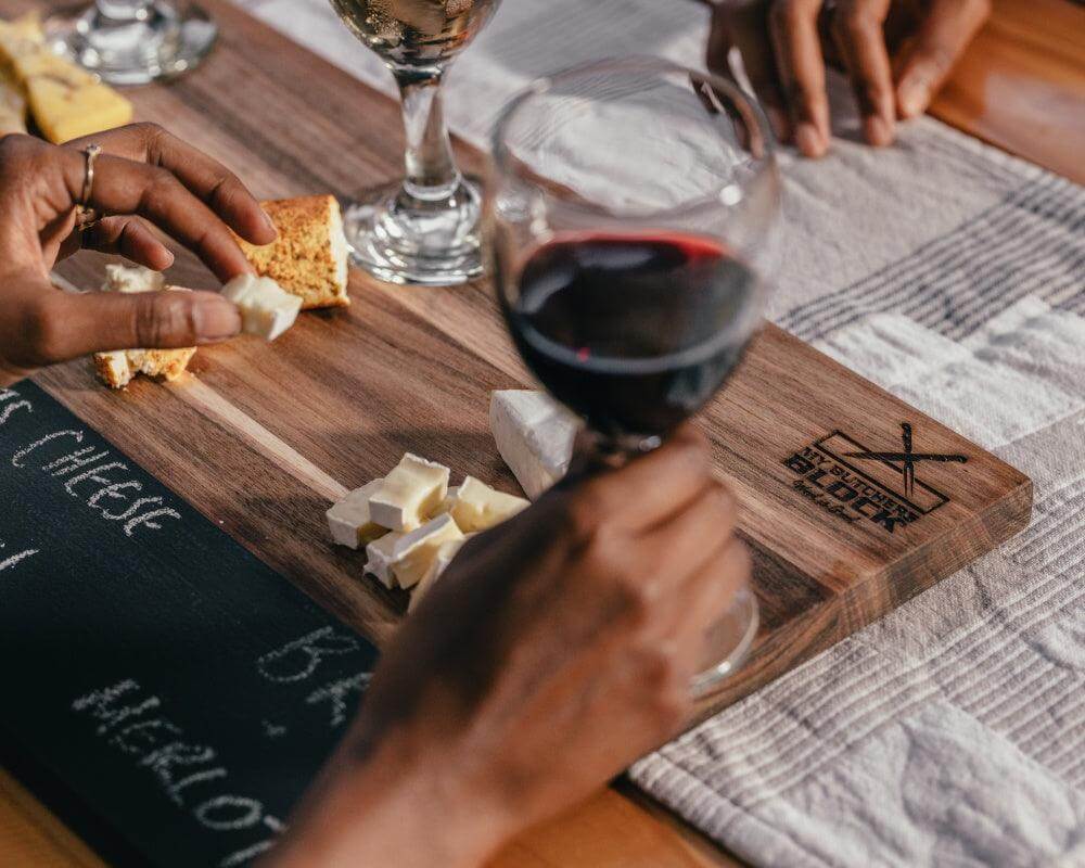 Hands enjoying wine and cheese on a Tasting and Pairing Board with a chalkboard inset for notes.