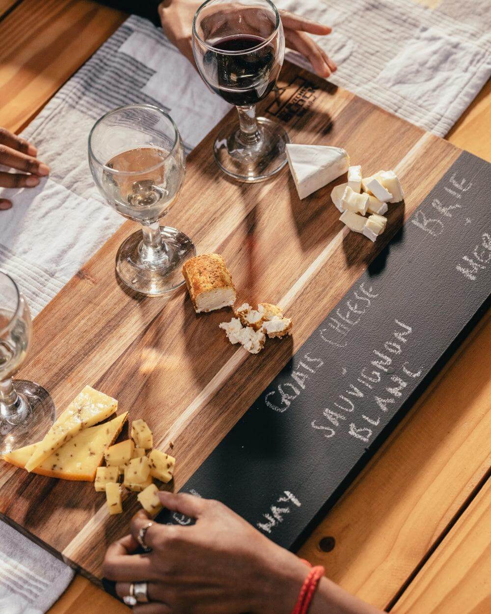 Tasting and Pairing Board with assorted cheeses, wine glasses, and handwritten pairings on a chalkboard inset.
