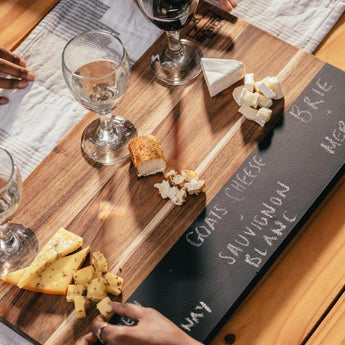 Tasting and Pairing Board with assorted cheeses, wine glasses, and handwritten pairings on a chalkboard inset.