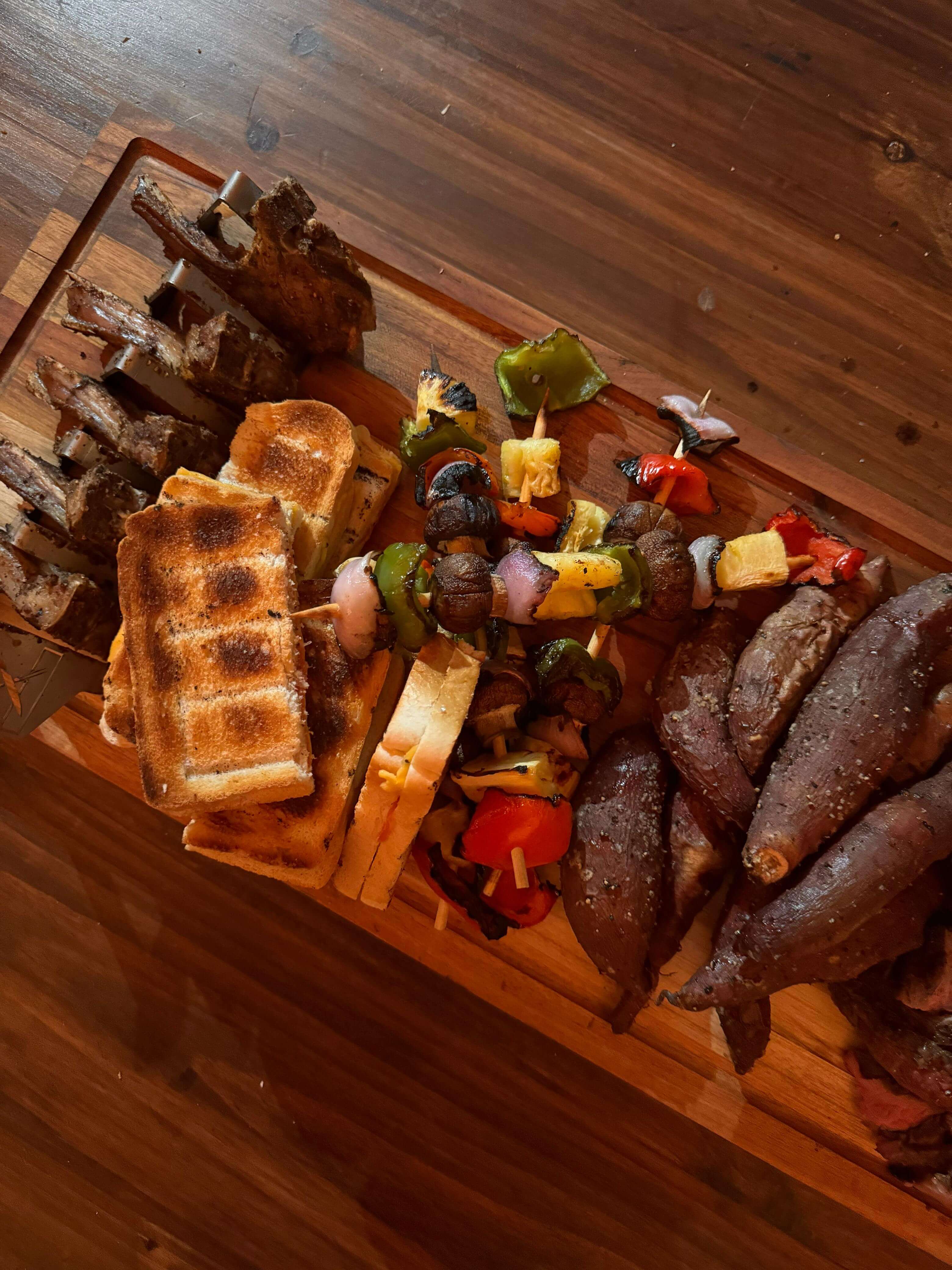 Grilled meats and vegetables served on a wooden cutting board, showcasing a delicious braai platter.