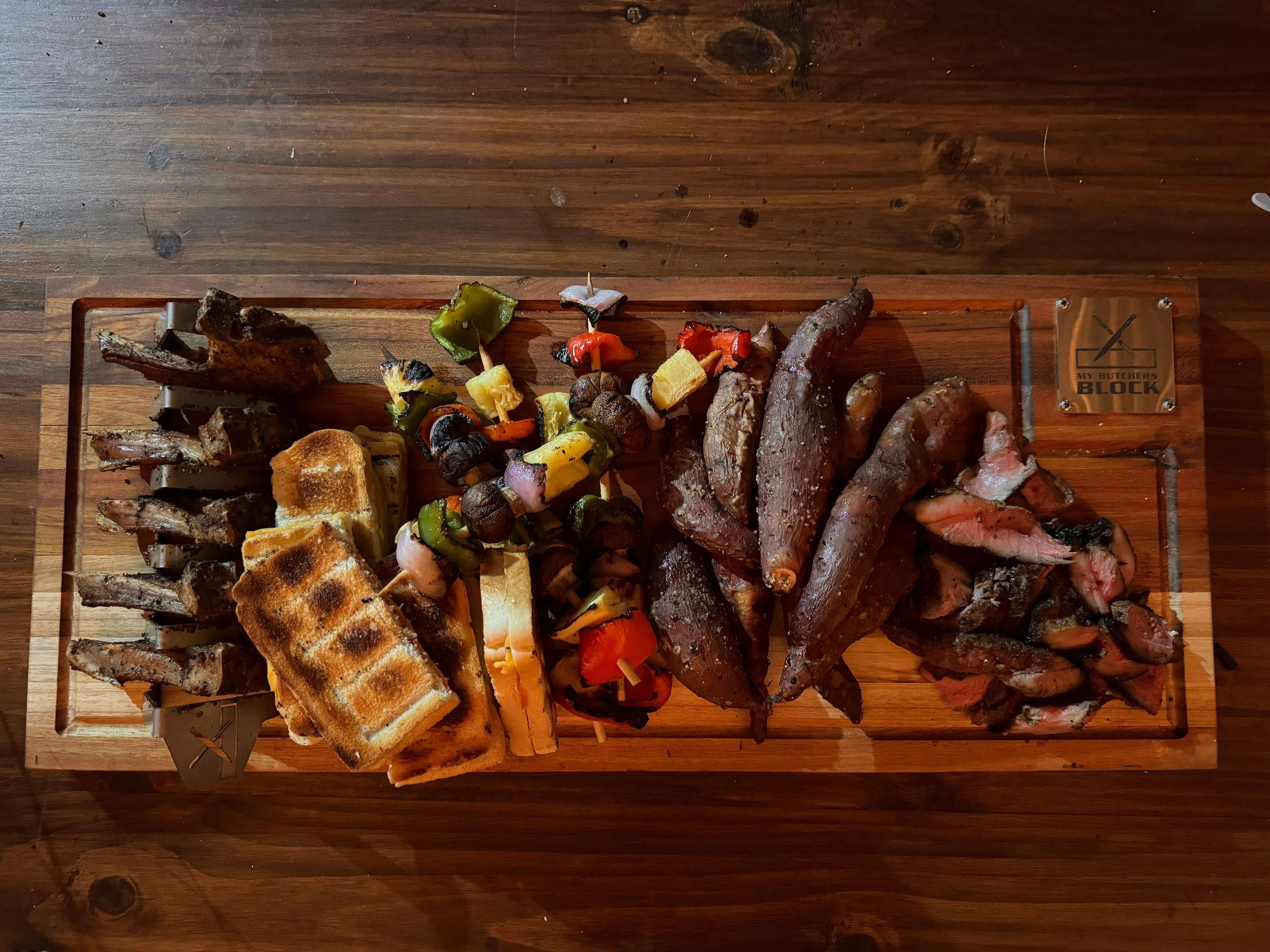 Delicious assortment of grilled meats, vegetables, and sweet potatoes on a wooden braai and slice master block.