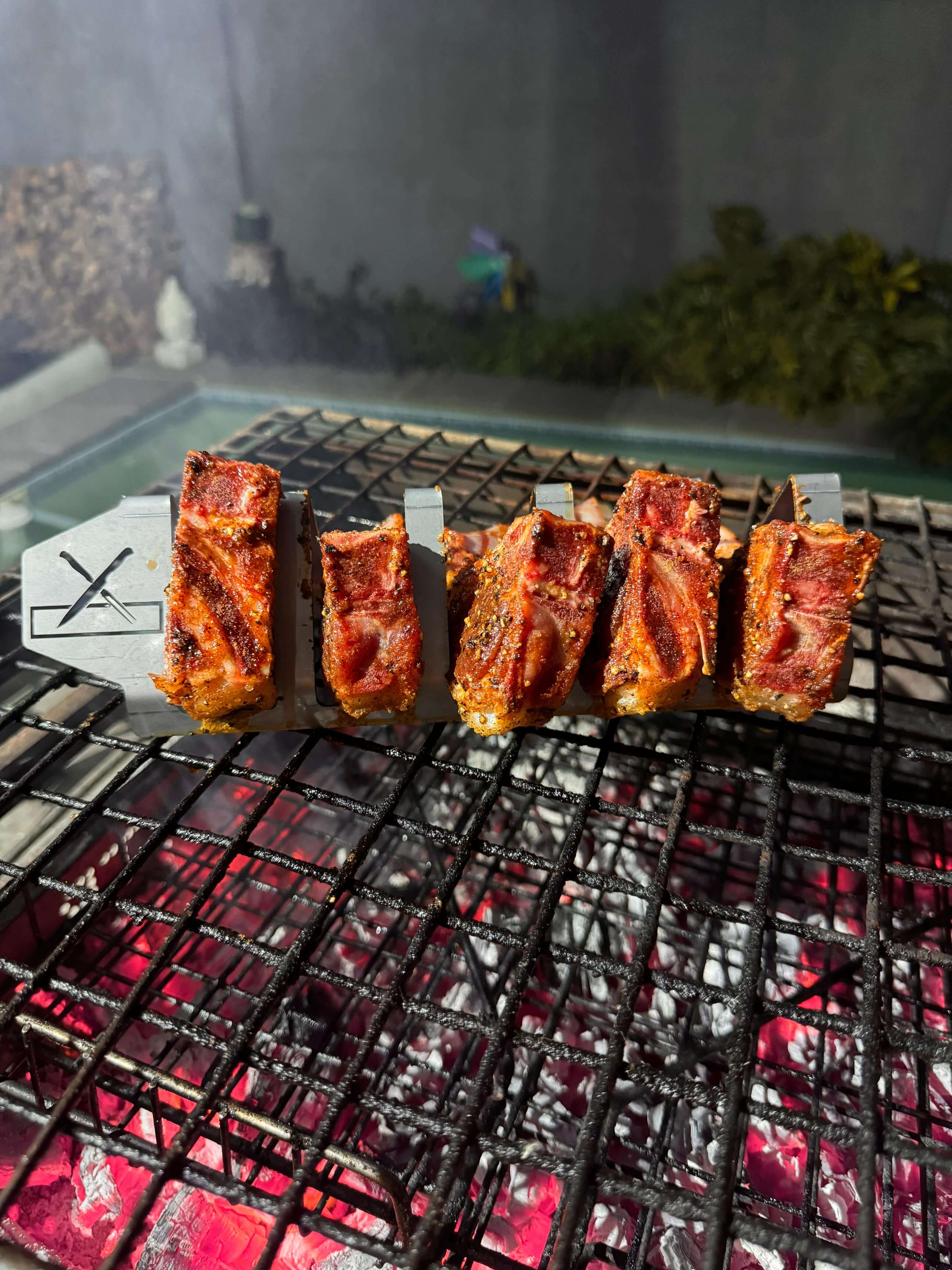 Grilled meat resting on a Braai and Slice Master Block grilling rack over glowing coals.
