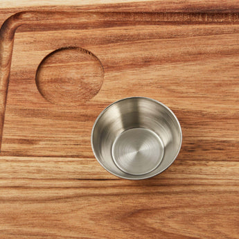 Close-up of a sleek stainless steel bowl on a wooden steak board, perfect for serving sauces and spices.