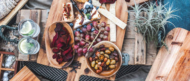 A beautifully arranged picnic spread featuring fruits, snacks, and drinks on wooden cutting boards.