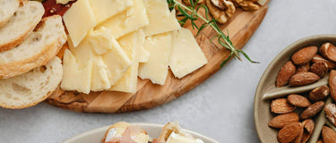 A beautifully arranged cheese board featuring various cheeses, bread, nuts, and pickles, perfect for gatherings.