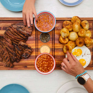How to Create the Perfect Plankie Braai with juicy meat, baked potatoes, beans, and eggs on a wooden platter.