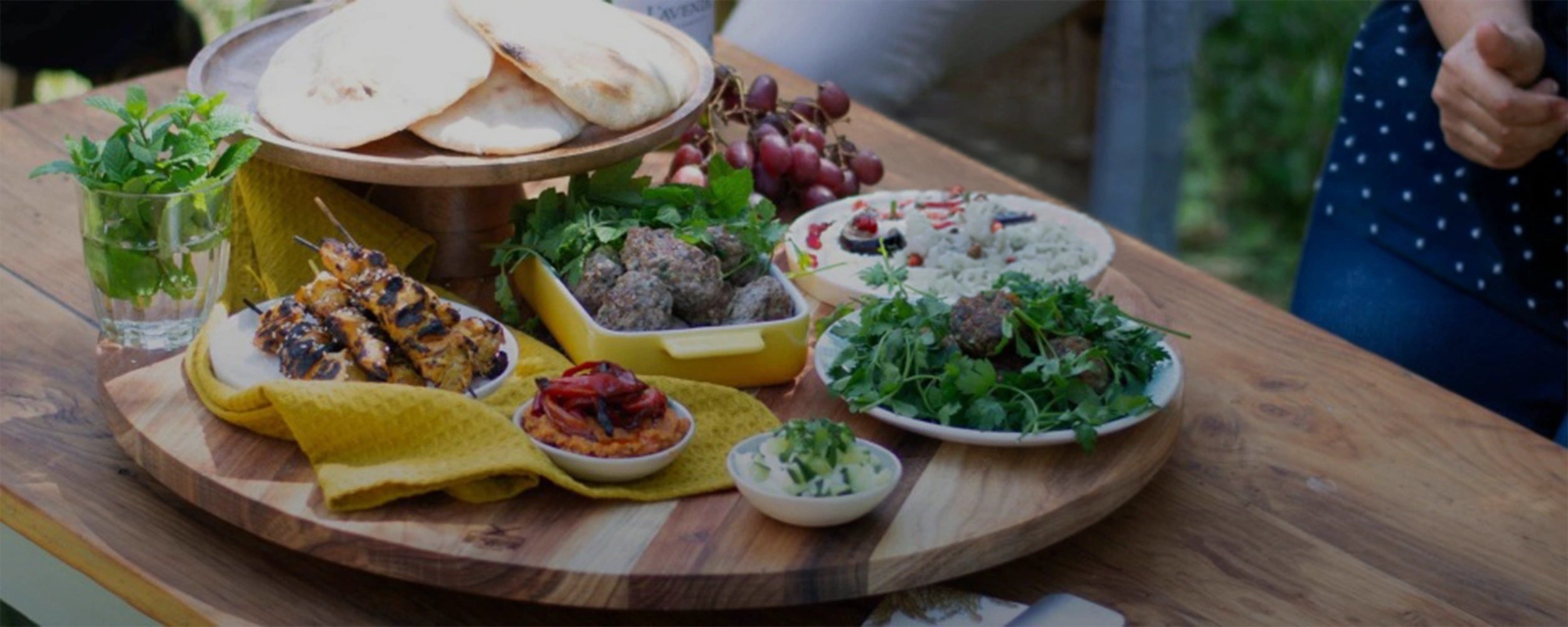 Assorted food platter on a wooden table with a person partially visible.