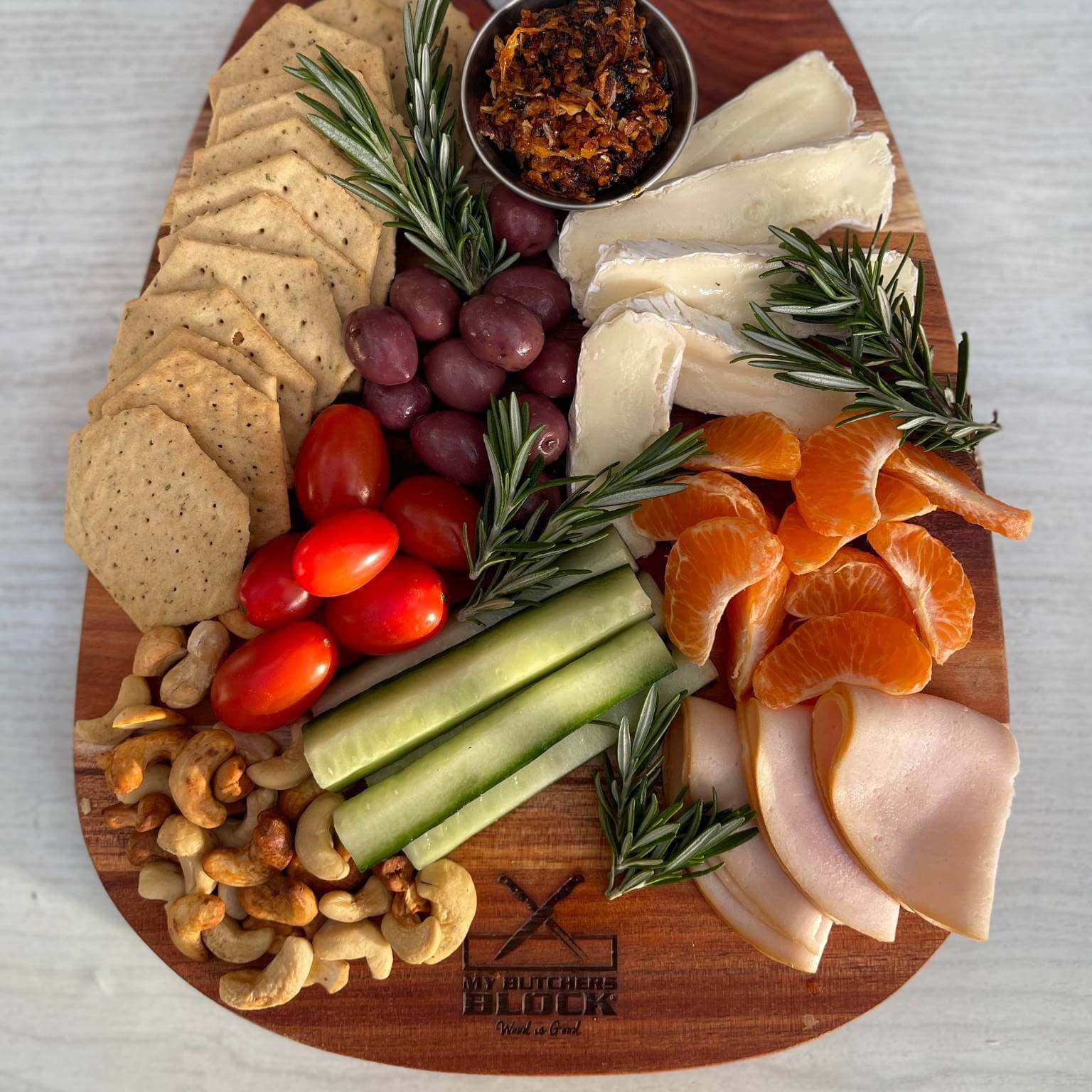 Beautifully arranged charcuterie on a small paddle board featuring crackers, olives, cheese, fruit, and nuts.