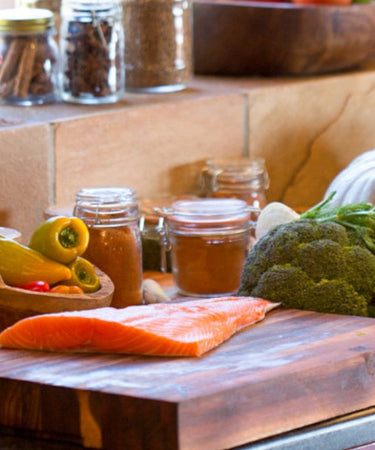 Fresh ingredients on a rustic kitchen counter with vegetables, spices, and salmon ready for cooking.